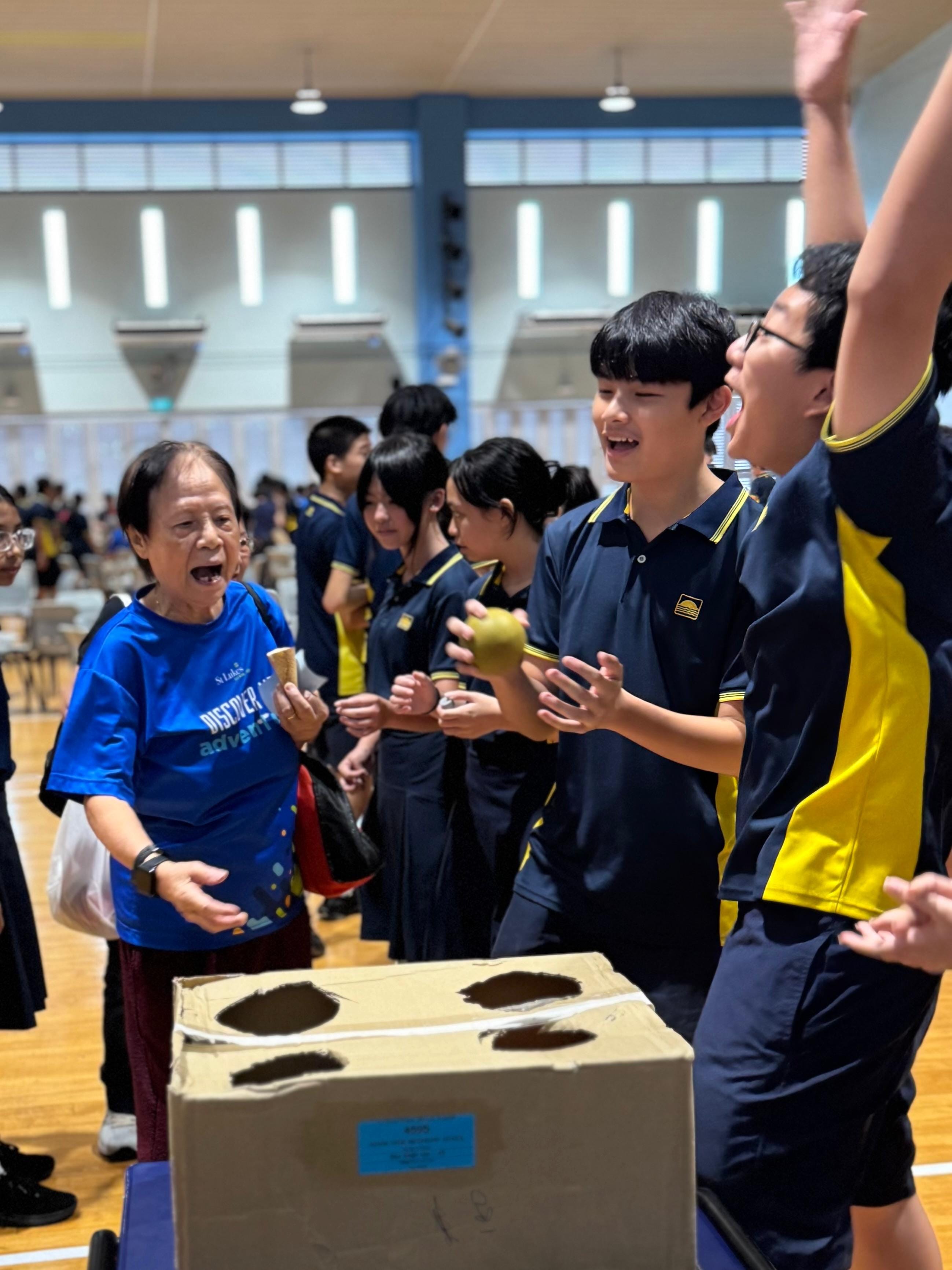 Two smiling students in navy and yellow uniforms hold a handwritten planning sheet with tables and notes.
